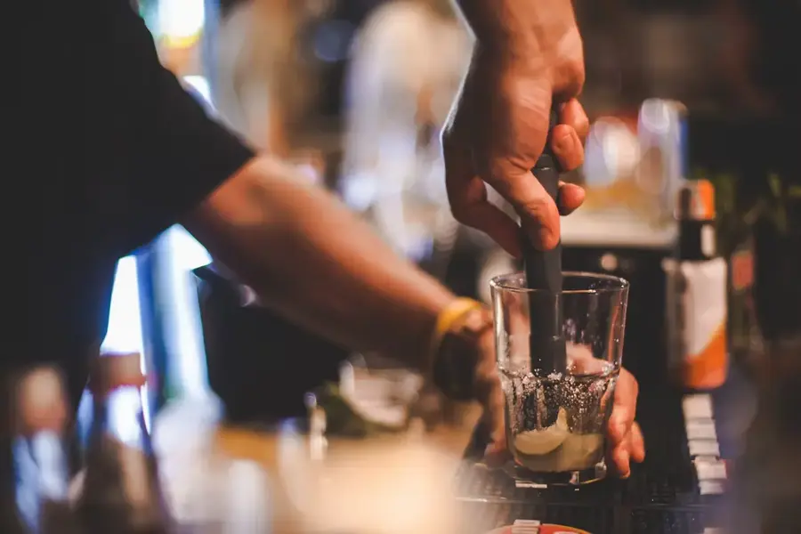 Bartender muddling ingredients in a glass at a bar